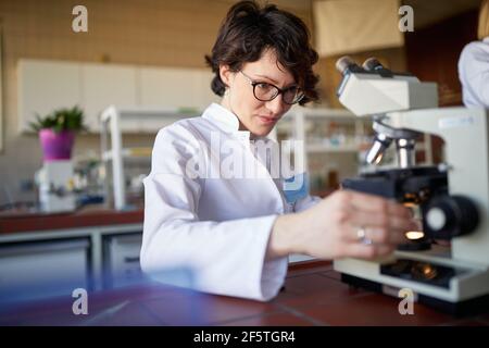 A young female scientist adjusts the microscope in a working atmosphere at the university laboratory. Science, chemistry, lab, people Stock Photo