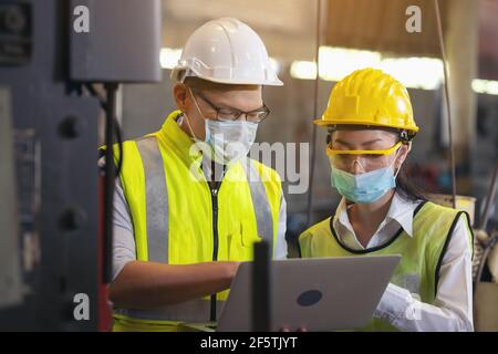 Two engineer in hard hat wearing safety using laptop for planning a project. Foreman explaining machinery to female employee Stock Photo