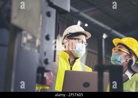 Two engineer in hard hat wearing safety using laptop for planning a project. Foreman explaining machinery to female employee Stock Photo