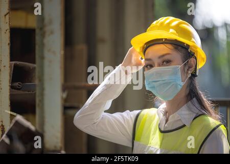 A portrait of an industrial woman engineer with mask standing in a factory. Work at the Heavy Industry Manufacturing Facility concept. Stock Photo