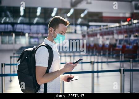 Travel in new normal. Man using mobile app at airport. Passenger wearing face mask and holding smart phone with passport. Stock Photo