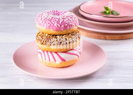 Three iced donuts are stacked on a pink ceramic plate Stock Photo