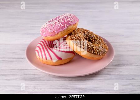Three sugar-coated donuts are stacked on a pink ceramic plate Stock Photo