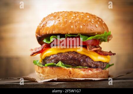 burger with cheese, bacon, salad and vegetables on a wooden  board Stock Photo