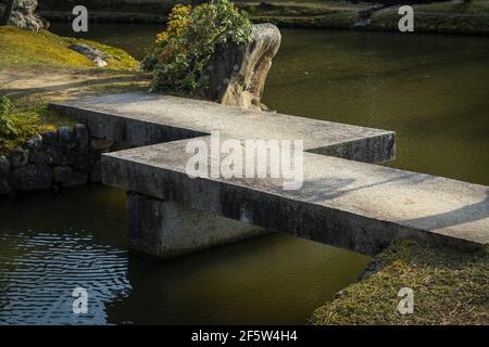 Geometric concrete zig-zag bridge over a pond in a Japanese garden 
