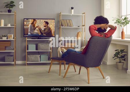 Relaxed woman sitting in chair in living-room and watching soap opera on television Stock Photo