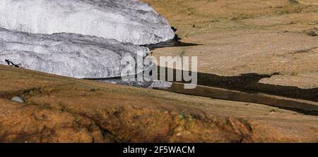 Warm spring sunlight melting ice forming small creek over rocks Stock Photo