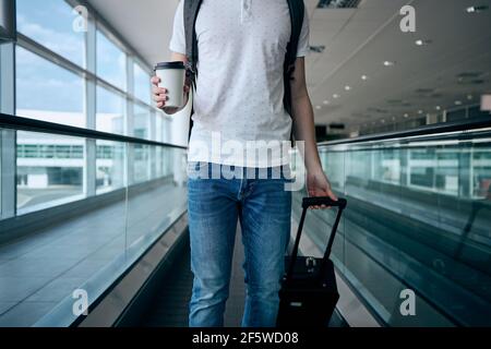 Man walking with paper coffee cup. Front view of traveler on moving walkway at airport terminal. Stock Photo