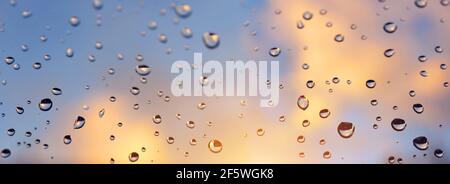 Water drops on a window glass after the rain at sunset. Panoramic nature background. Stock Photo
