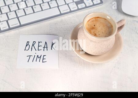 Break time. Concept time off. Words BREAK TIME in note on the working table with cup of coffee and keyboard. Top view. Stock Photo