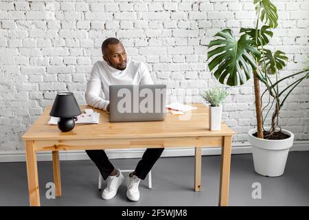 Focused male freelancer is using laptop, sitting at the desk in home office. Serious businessman lost in thoughts, looking at the side, working on new Stock Photo