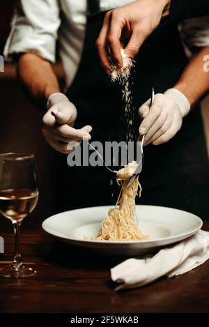 Close-up of the chef's hand pouring grated cheese onto the pasta Stock Photo