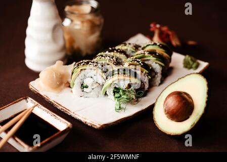 Close-up of a set of sushi rolls with an avocado cut in half lying next to it