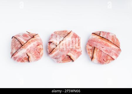 Close-up of chicken burgers wrapped in bacon ribbons. Semi-finished product for home use and gastro. Stock Photo