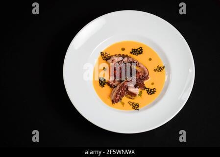 Pumpkin cream soup with octopus and croutons in a white bowl Stock Photo