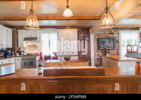 B.C. fir general store long counter and white pine wood cabinets in kitchen with pendant lighting fixtures inside an old circa 1790 Canadiana home Stock Photo