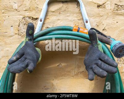Close-up photography of an used pair of rubber and fabric gloves and a hose hanging from the wall of a house near the colonial town of Villa de Leyva, Stock Photo