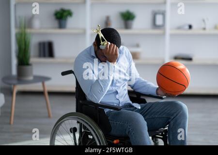 Young black basketball player in wheelchair holding ball and feeling stressed over his injury at home Stock Photo