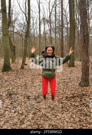 Smiling, happy and positive girl in the park among the trees enjoys life. A woman in a sports outfit, jumps up, is exercising outdoors Stock Photo