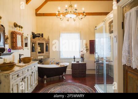 Bleached antique wooden general store cabinet with two molded bowl sinks, claw foot bathtub and clear glass shower stall with blue, white ceramic tile Stock Photo