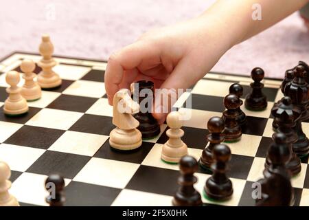 Little childs hand moving a rook chess piece on a chessboard, closeup. Clever anonymous child making a move in a game of chess, capturing a piece. Int Stock Photo