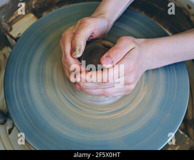 Teenage hands over the potter's wheel. Sculpt from clay in a pottery workshop. Traditional pottery craft. Ceramics workshop concept Stock Photo