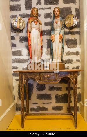 Painted wooden religious sculptures on table against natural stone chimney wall in upstairs hallway inside an old circa 1790 Canadiana cottage home Stock Photo