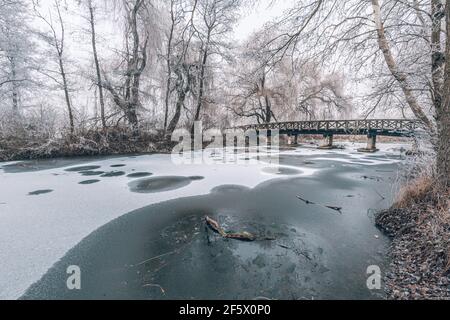 Snowy, wooden bridge in a winter day. Frozen lake and snowy trees, idyllic seasonal winter scenery. Winter landscape, relaxing and calmness view Stock Photo