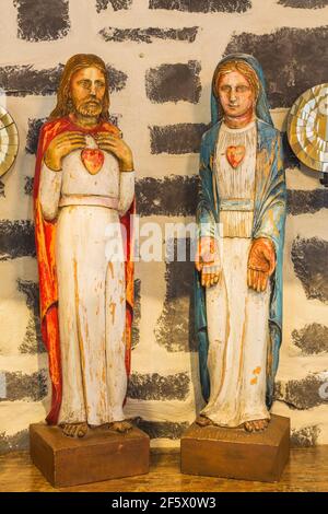 Painted wooden religious sculptures on table against natural stone chimney wall in upstairs hallway inside an old circa 1790 Canadiana cottage home Stock Photo