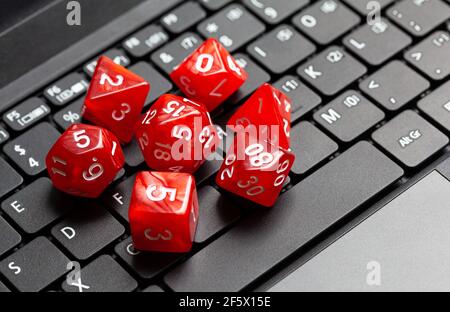 Set of simple red RPG role playing fantasy board game dice laying on a modern laptop computer keyboard, closeup, from above, nobody. Online rpg pc gam Stock Photo