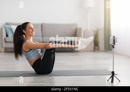 Active woman sitting on yoga mat, watching fitness video Stock Photo