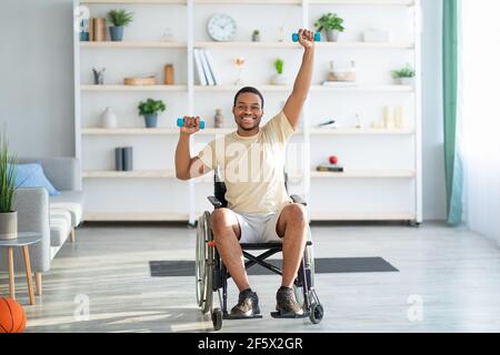 Physical activities for disabled people. Handicapped man in wheelchair making rehabilitation exerises with dumbbells Stock Photo