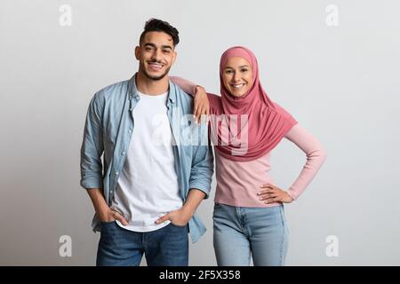 Happy arab man and young woman in hijab posing over gray background Stock Photo