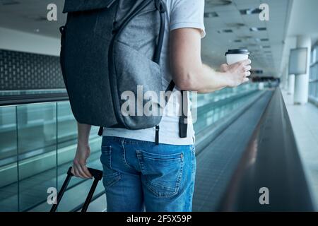 Man walking with paper coffee cup. Traveler on moving walkway at airport terminal. Stock Photo