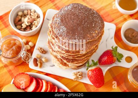 Pancakes tower with powdered sugar and fruit. Strawberries, apples, nuts and jam. Stock Photo