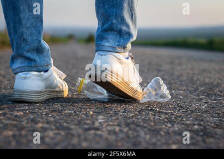 Legs crush plastic bottle on the road. Environmental conservation. Plastic waste Stock Photo