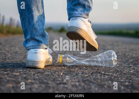 Legs crush plastic bottle on the road. Environmental conservation. Plastic waste Stock Photo