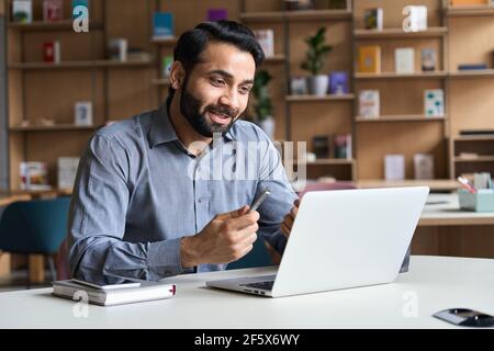 Young indian business man talking, having virtual meeting working on laptop. Stock Photo