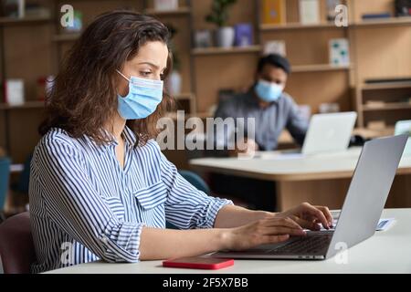 Latin girl student wearing face mask studying on laptop with diverse people. Stock Photo