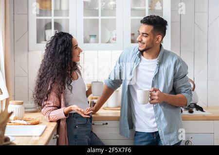 Cheerful Middle Eastern Couple Relaxing In Kitchen Together, Drinking Coffee And Chatting Stock Photo