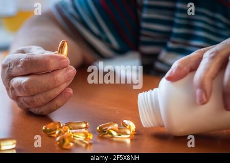 Senior woman taking omega 3 capsule from bottle. Medical and healthcare concept. Food supplement Stock Photo