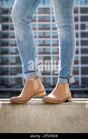 Fashionable slim legs wearing jeans and leather shoe in city. Modern architecture as background. Stylish woman wearing casual clothing standing on wal Stock Photo