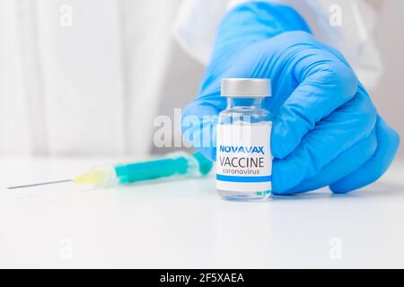 Novavax vaccine against coronavirus and syringe for injection on the table and health worker hand in rubber gloves and protective suit on the Stock Photo
