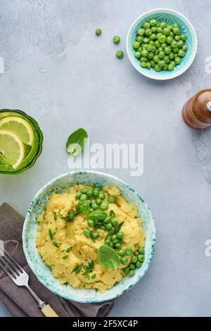 Mashed potato with butter, green peas, onions, basil in a white bowl on a light slate, stone or concrete background. Top view with close up. Stock Photo