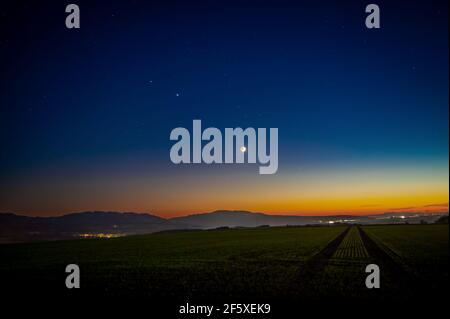 A beautiful shot of rising Saturn, Jupiter and moon over meadow after sunset Stock Photo