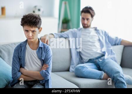 Family generations conflict. Upset boy and father not talking after quarrel, son and dad sitting on couch separately Stock Photo