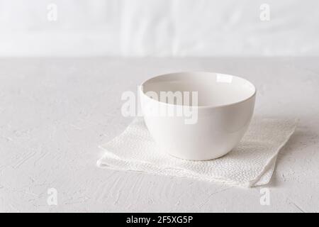 White empty bowl on a white rough surface close-up. Empty ceramic cup against light background. Clean porcelain soup bowl on table. Food design mockup Stock Photo