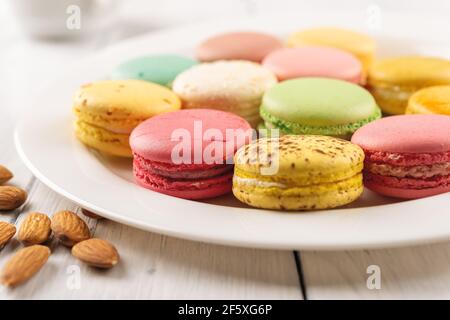 Closeup of tasty multicolored macaroons on a white porcelain plate. Sweet breakfast with delicious almond meringue cookies. Colorful macaron cakes. Stock Photo