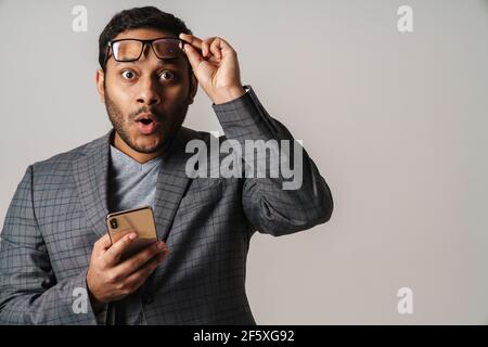 Asian surprised businessman looking at camera and holding cellphone isolated over gray background Stock Photo