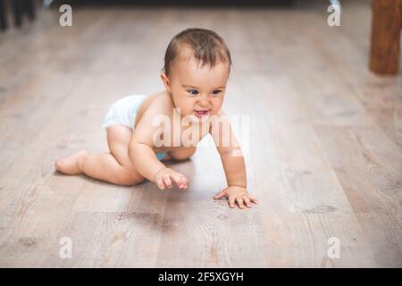 Small adorable infant standing on all fours on wooden floor at home. Stock Photo